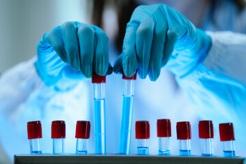 Scientists in lab coats and gloves pour blue liquid from one test tube to another to perform...