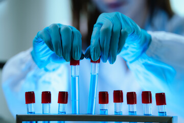 Scientists in lab coats and gloves pour blue liquid from one test tube to another to perform...