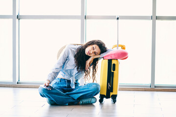 Young woman resting at airport terminal with suitcase and travel essentials, dressed casually for a...