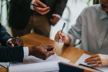 Professionals gather around a wooden table engaging in a discussion during a business meeting,...