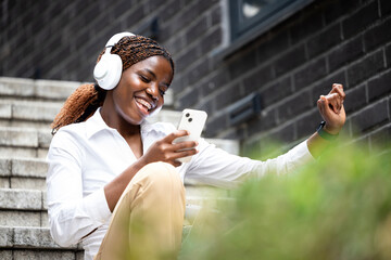 Cheerful African woman listening to the music and using smart phone