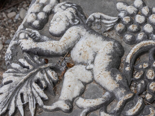 Bas-relief on the surface of a stone block in the ancient city of Perge in Turkey. An image of an angel and grapes on a stone surface. Grape leaves and berries next to an angel on a stone.