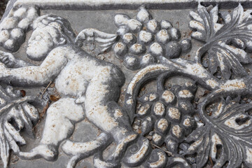 Bas-relief on the surface of a stone block in the ancient city of Perge in Turkey. An image of an angel and grapes on a stone surface. Grape leaves and berries next to an angel on a stone.