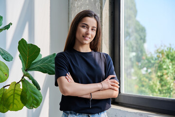 Portrait of confident successful teenage girl posing with crossed arms near window