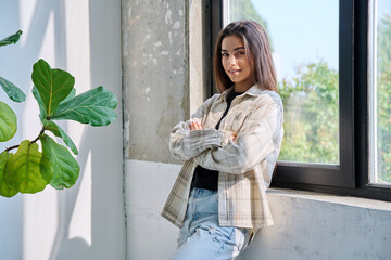 Portrait of confident successful teenage girl posing with crossed arms near window