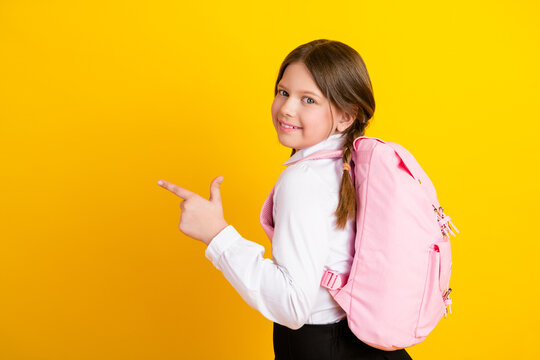 Smiling girl with backpack gesturing hand sign, prepared for school on yellow background, youthful energy and enthusiasm