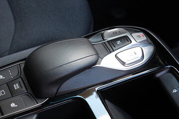 Gear shift buttons in electric car. Gear lever close up. Car interior details made of grey textile and leather. Car central console with cup holders. Transmission shift. Black leather car interior.