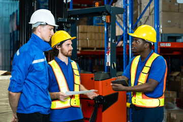 Multiracial group of adult male warehouse workers discussing checklist task together near forklift...