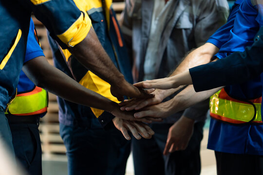 A diverse group of warehouse workers, including both white and black men, hold hands, demonstrating unity, teamwork, strength, and cooperation within the industrial workplace., logistics warehouse. - Powered by Adobe