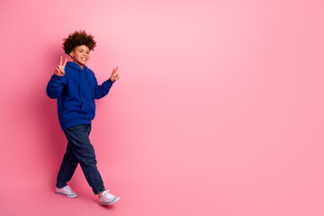 Stylish young boy in blue hoodie showing peace gestures on a pink backdrop, expressing joy and positive energy