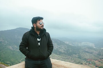 Man in sunglasses enjoys panoramic Nandi Hills view, Karnataka, India. Serene landscape composition.