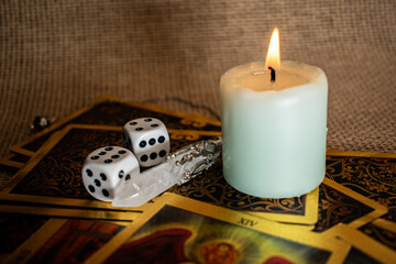 Tarot cards with vivid illustrations lie on burlap, with a quartz pendulum and a lit candle. A...