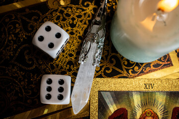 Tarot cards with vivid illustrations lie on burlap, with a quartz pendulum and a lit candle. A...