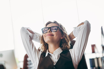 Young businesswoman enjoying relaxation in stylish office environment seated on chair with hands...