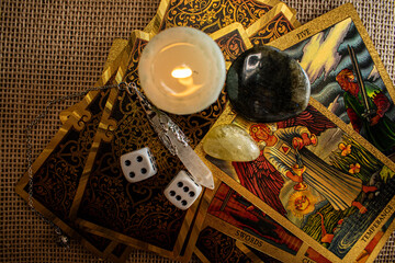 A soft blue candle burns on tarot cards, with dice, quartz, citrine, and labradorite on burlap. A...
