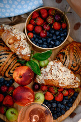 Summer picnic with fresh berries, fruits, almond croissants, and rosé wine on a cozy blanket. Flat lay top view, bright and seasonal outdoor setup.