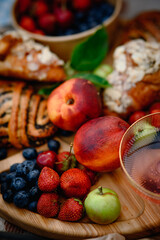 Summer picnic with fresh berries, fruits, almond croissants, and rosé wine on a cozy blanket. Flat lay top view, bright and seasonal outdoor setup.