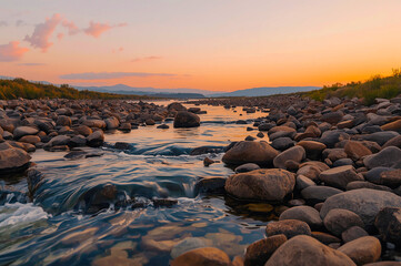 Obraz premium Sunset River with Rounded Rocks and Distant Mountain Horizon, Tranquil Nature Scene
