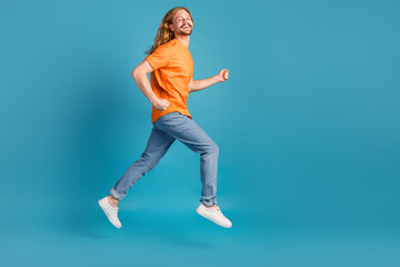 Cheerful young man jumping against a blue background wearing casual outfit and enjoying a joyful...