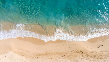 Aerial view of turquoise ocean meeting sandy beach with footprints and shadows