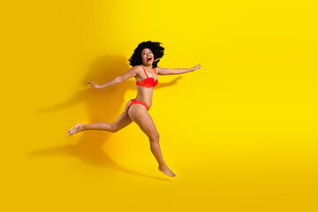 Energetic woman in vibrant red swimwear posing joyfully against a yellow background, showcasing...