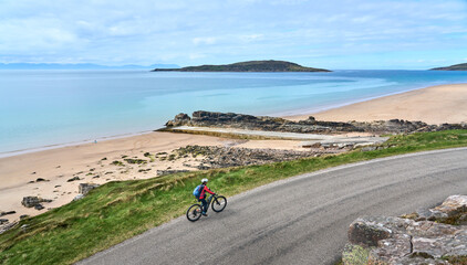 cheerful senior woman riding her electric mountain bike at a rocky beach of the scottiish Atlantic...