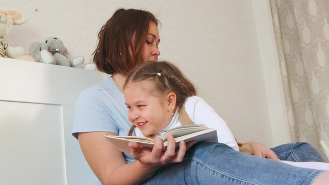 Caucasian mother reads a childrens book to her girl in bed. Preschool development and maternal care in a home learning space. Bottom view