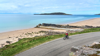 cheerful senior woman riding her electric mountain bike at a rocky beach of the scottiish Atlantic...