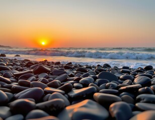 Obraz premium Sunset Over Pebbled Beach with Gentle Waves and Vibrant Orange Sky