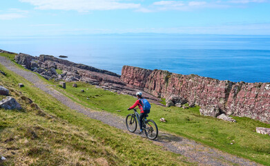 active senior woman riding her electric mountain bike on the cliffs near Rua Reidh Lighthouse next...