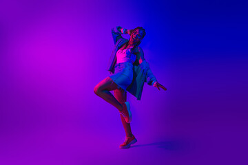 Energetic young woman dancing in vibrant neon light creating a fun and stylish atmosphere
