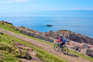 active senior woman riding her electric mountain bike on the cliffs near Rua Reidh Lighthouse next to  Gairloch in north western Scotland, UK