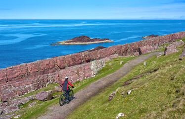 active senior woman riding her electric mountain bike on the cliffs near Rua Reidh Lighthouse next...