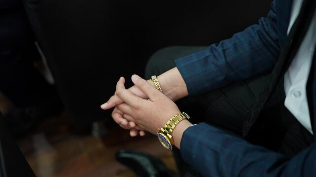 A top cinematic shot of a wealthy man wearing a gold bracelet and a luxury watch sitting confidently
