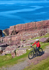 active senior woman riding her electric mountain bike on the cliffs near Rua Reidh Lighthouse next...