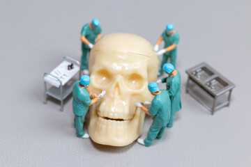 Tiny toy doctors in scrubs perform a delicate and precise surgery on a large human skull model,...