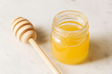 Fresh honey in a glass jar. Natural sweetness with honey dipper on marble background. Healthy organic product rich in nutrients. Golden liquid texture. Traditional ingredient for tea or breakfast.
