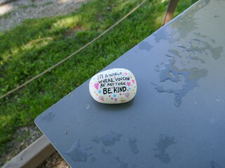 Be kind kindness rock on wet outdoor metal table