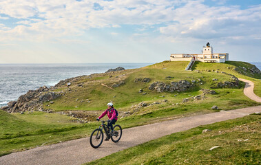 active senior woman riding her electric mountain bike at Strathy  point lighthouse in Northern...