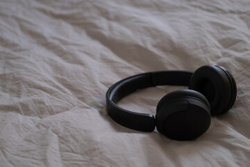 Black wireless headphones lying on beige bedding in natural light. 