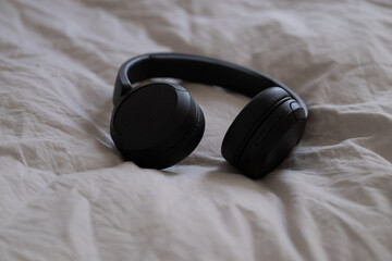 Black wireless headphones lying on beige bedding in natural light. 