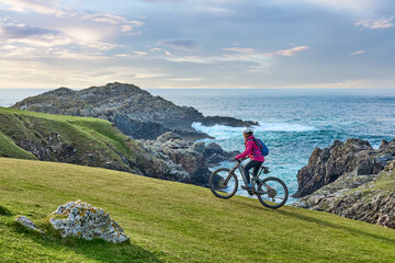 active senior woman riding her electric mountain bike at Strathy  point lighthouse in Northern...