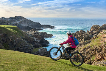 active senior woman riding her electric mountain bike at Strathy  point lighthouse in Northern...