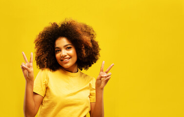 Cheerful young african american woman showing victory sign isolated on yellow color wall background