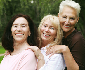 Old people, friendship and emotions concept: Three beautiful elderly ladies are hugging in the park. Women dressed in casual clothes have fun and feel happy.
