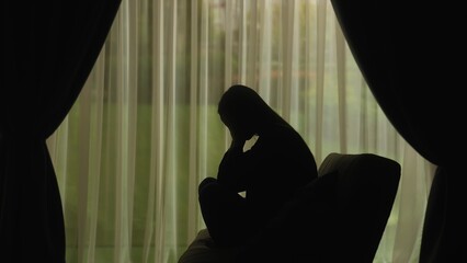 Silhouette of a distressed woman in front of backlit curtains