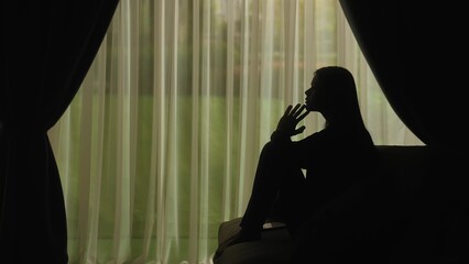 Silhouette of a distressed woman in front of backlit curtains