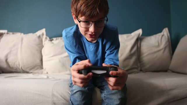  preteen boy with glasses with a joystick playing video game console sitting on the couch at home.  Generation Z.  gambling addiction