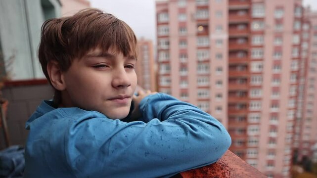 A sad teenage boy stands on the balcony and looks at the rain. the crisis of adolescence. teenage depression.