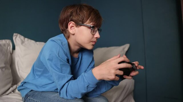  preteen boy with glasses with a joystick playing video game console sitting on the couch at home.  Generation Z.  gambling addiction